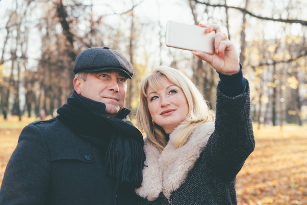 행복 한 금발 성숙한 여자와 아름 다운 중 년 갈색 휴대 전화에 selfie를 가져가 라.