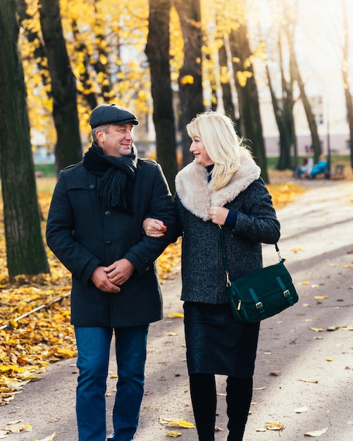 Happy blonde mature woman and handsome middle-aged brunette man walk in park