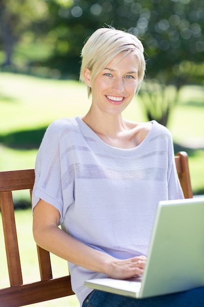 Happy blonde using laptop in a park 