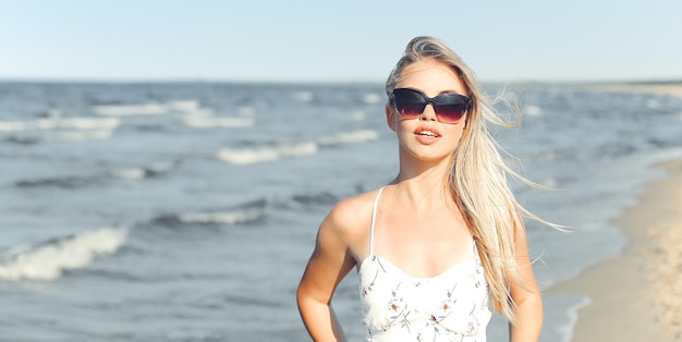 Happy blonde woman in free happiness bliss on ocean beach standing with sun glasses.