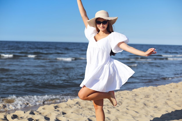 Happy blonde woman having fun on the ocean beach in a white dress and sunglasses.