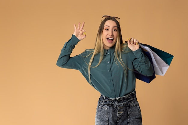 Happy blonde woman holding shopping bags with purchases and showing Ok gesture