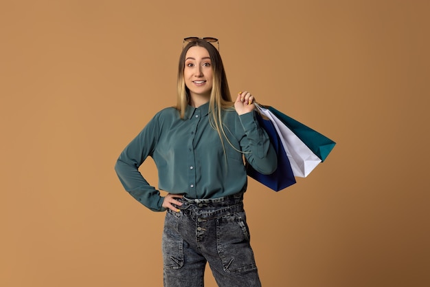 Happy blonde woman holding shopping bags with purchases on studio background.