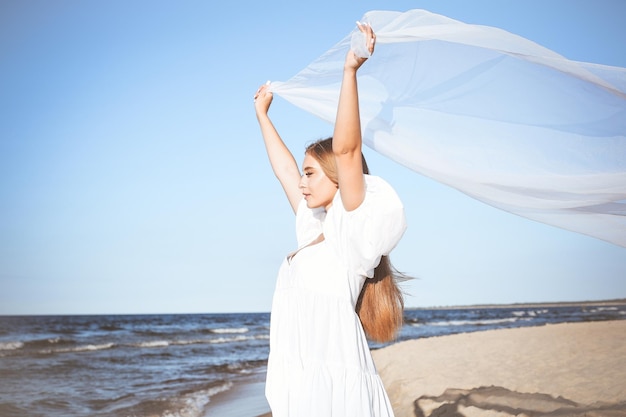 Happy blonde woman is catching clouds and wind with her arms on the ocean beach.