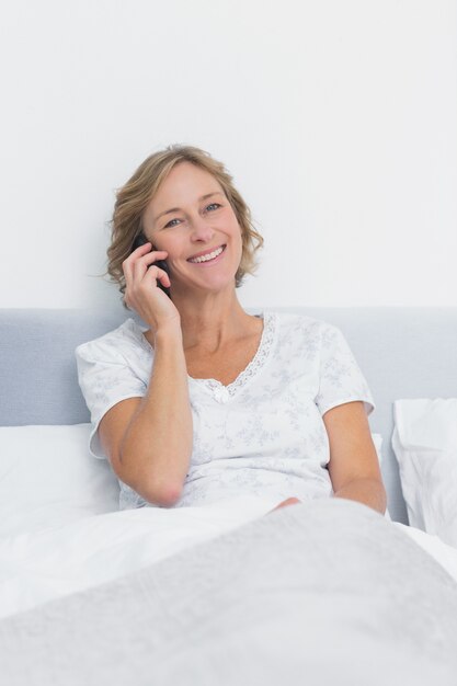 happy blonde woman on the phone in bed smiling at camera
