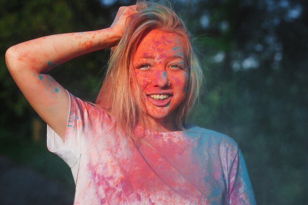 Счастливая блондинка играет с сухой краской colofrul на летнем фестивале Холи