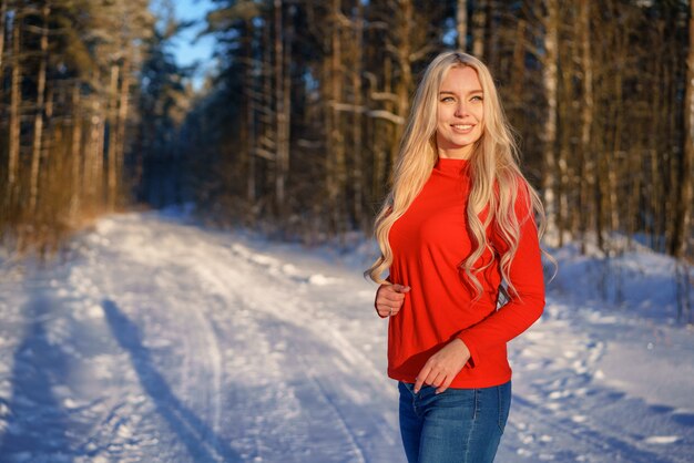 Happy blonde woman in red sweater in winter forest