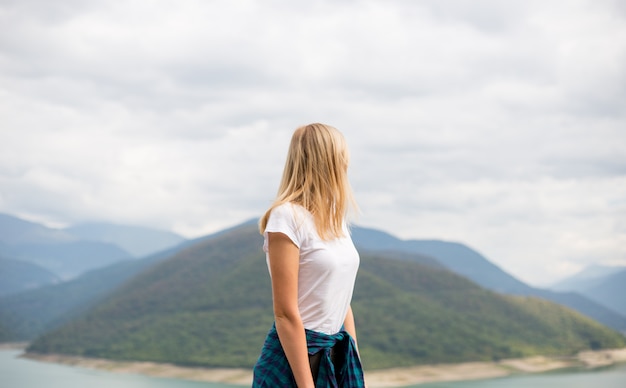 Happy blonde woman stands on the wall of mountain peaks. Ecotourism, travel concept and discovery of beautiful places