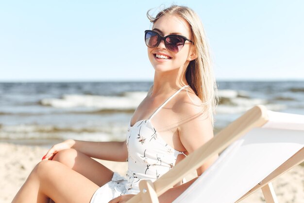 太陽眼鏡をかぶって海辺の木製のデッキチェアでリラックスしている幸せな金の女性