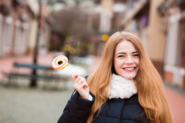 Happy blonde woman with long hair holding colorful lollipop at the city background