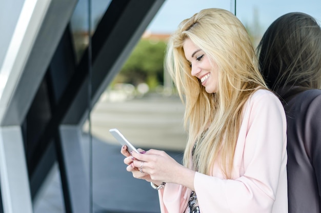 幸せな金の若い女性が外で携帯電話を使って孤立しています