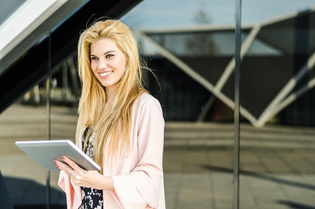 Happy blonde young woman outdoor using her tablet