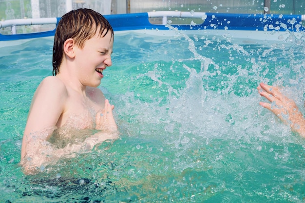 Happy boy bathes in pool with splashes on hot summer day