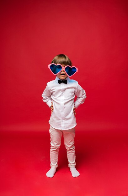 Happy boy in big funny heart shaped glasses on red