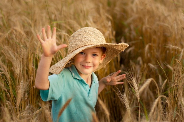 Foto ragazzo felice in grande cappello di paglia sul campo agricolo