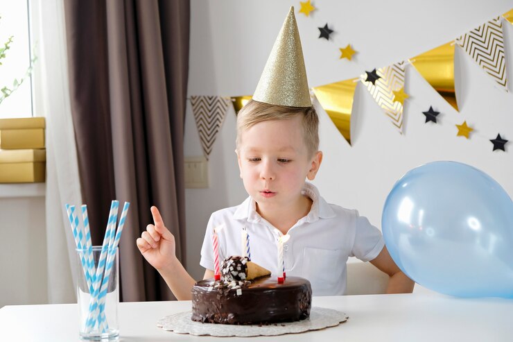 Happy boy celebrating birthday and blowing lighting candles on a cake