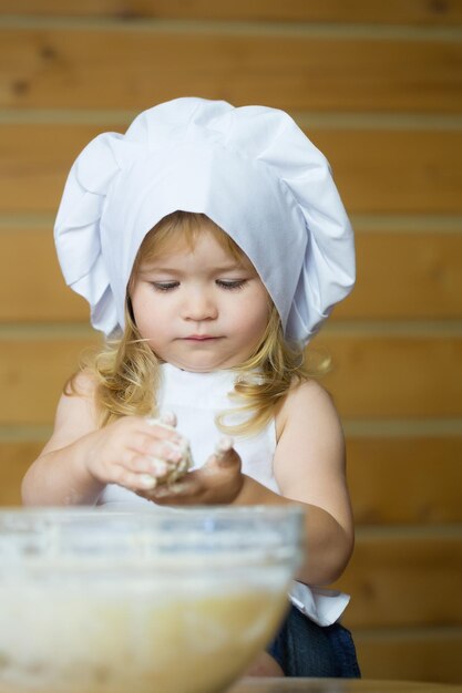 幸せな男の子の子供は生地をこねる料理人