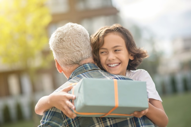 Ragazzo felice. ragazzo sveglio che tiene un regalo e che abbraccia suo padre