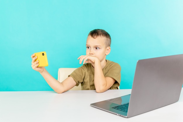 Happy boy at the distance education talking someone phone and using computer to study.