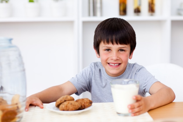 幸せな少年はビスケットを食べ、牛乳を飲む