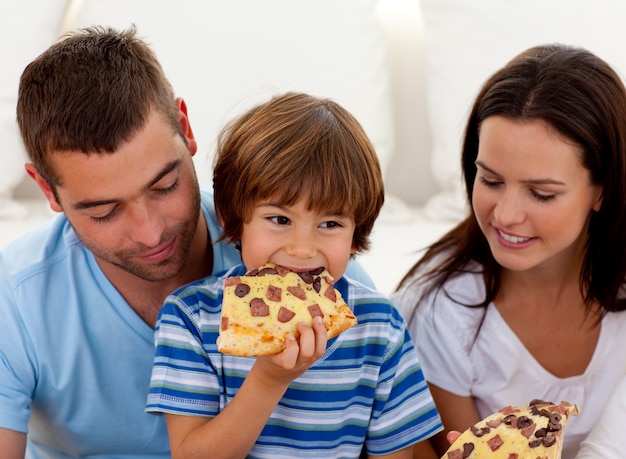Счастливый мальчик ест пиццу с их родителями