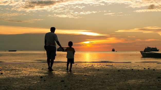 Ragazzo felice e padre che camminano sullo sfondo tramonto spiaggia