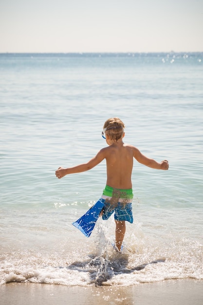 Happy boy in flippers running into ocean on a sunny day Child going to swim in the sea Vacations