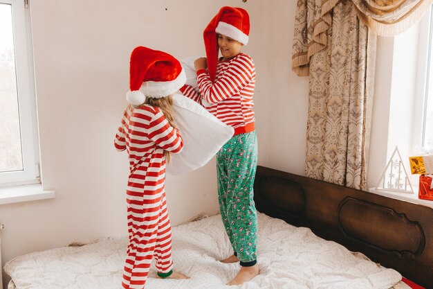 Foto felice ragazzo e ragazza in cappelli di natale la mattina di natale giocano e combattono con i cuscini a letto