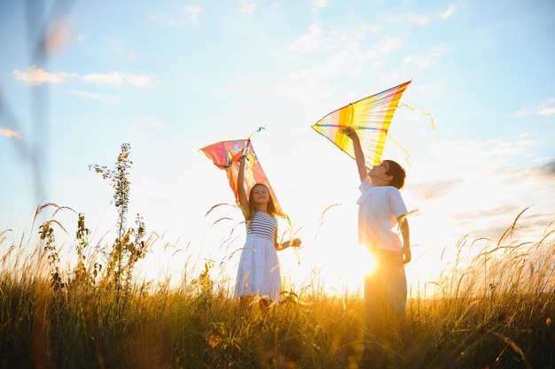 Happy boy and girl playing with kites in field at sunset Happy childhood concept