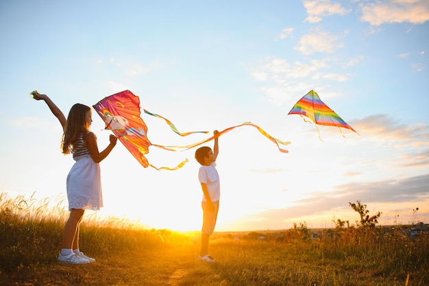 Happy boy and girl playing with kites in field at sunset happy\
childhood concept