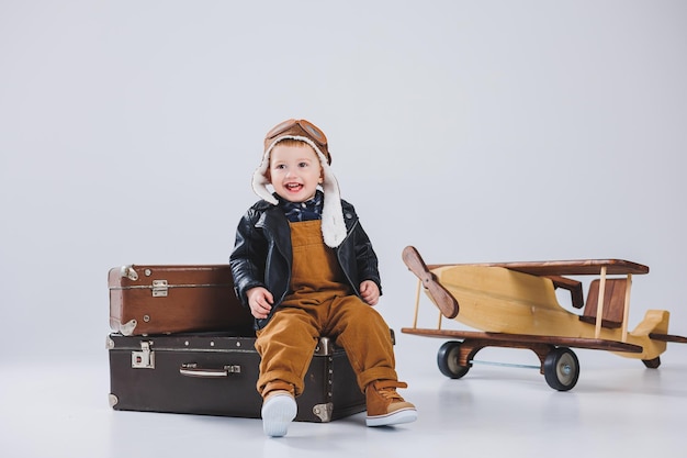 A happy boy in a helmet and a pilot's jacket stands near a wooden plane Portrait of a child pilot a child in a leather jacket Wooden Toys Eco plane from tree