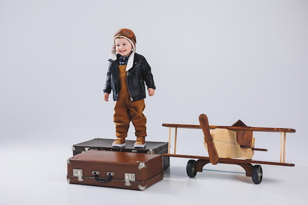 ヘルメットとパイロットのジャケットを着た幸せな少年が木製の飛行機の近くに立っている革のジャケットを着た子供のパイロットの肖像木から木のおもちゃエコ飛行機