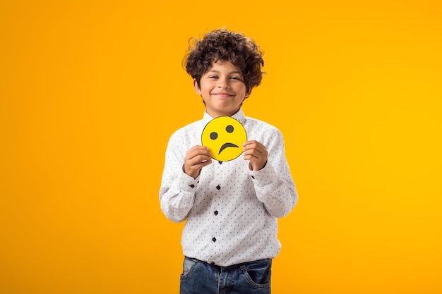 Счастливый мальчик держит счастливые и грустные лица на двух кусочках бумажного смайлика