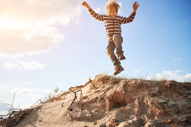 Happy boy jumping on sand at sunny day