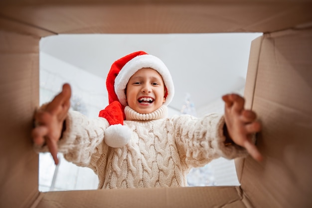 Happy boy in a knitted and Santa hat looks into the box