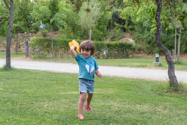 Happy boy leaning and throwing yellow paper airplane on bright sunny day in the field