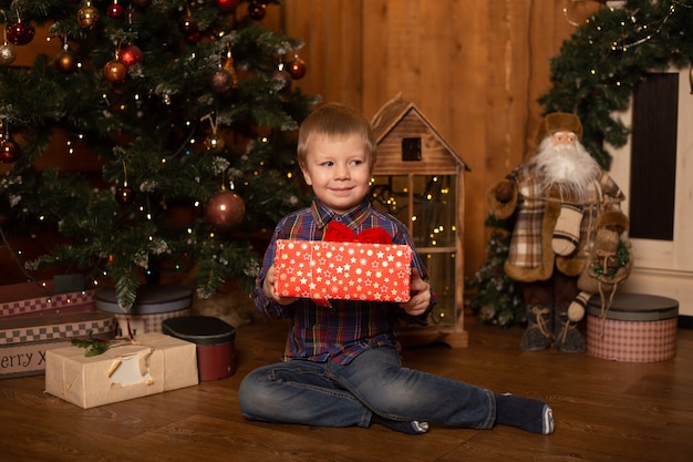 Happy boy near Christmas tree with gifts in his hands