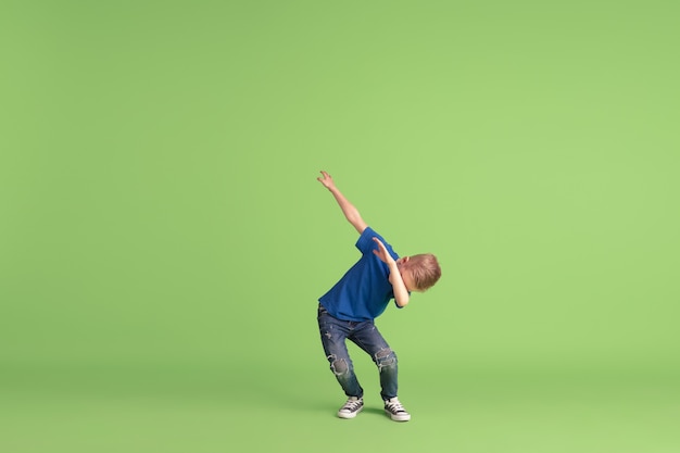 Happy boy playing and having fun on green studio wall