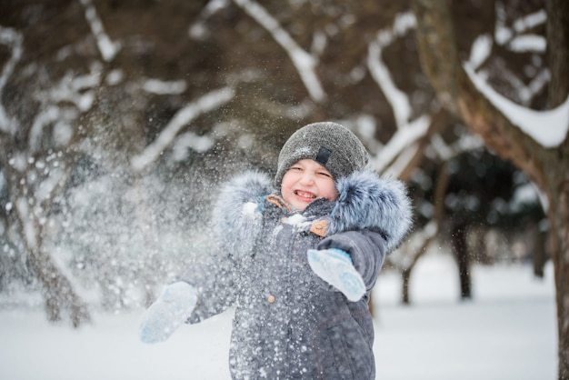 Счастливый мальчик играет в снегу, зимние игры