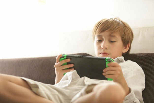 Счастливый мальчик играет в видеоигру, сидя на диване