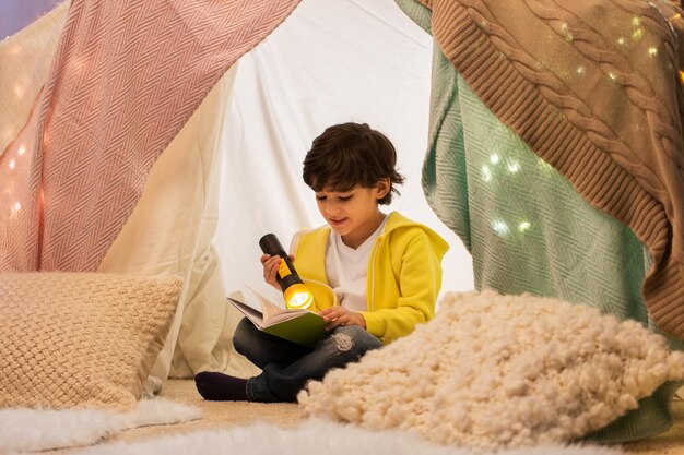 happy boy reading book in kids tent at home