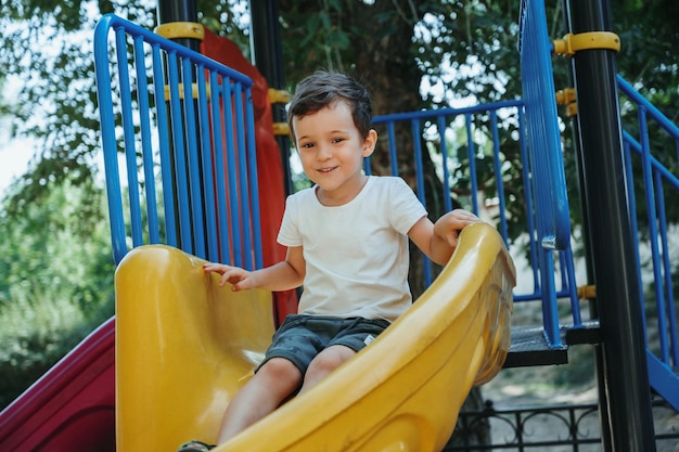 happy boy rides a slide on the playground in summer