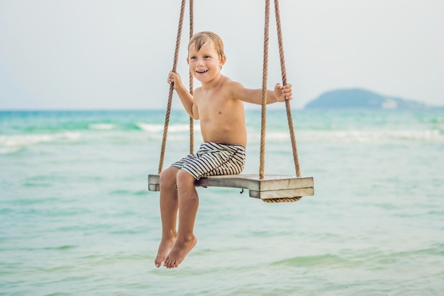 Happy boy sit on swing at the sea shore on sunset