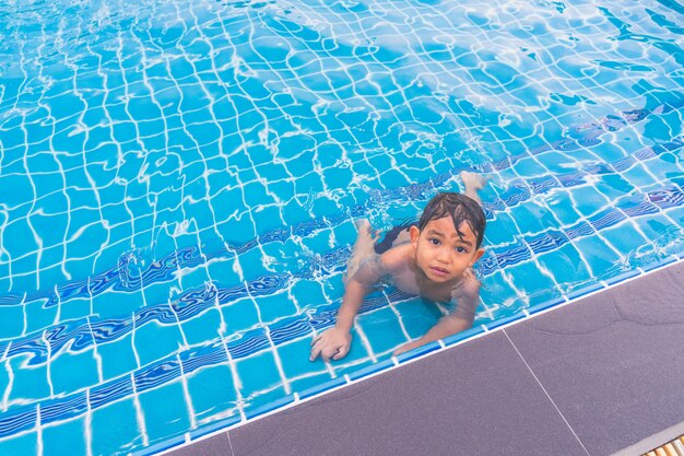 Foto ragazzo felice che si siede intorno alla piscina e alla ricerca