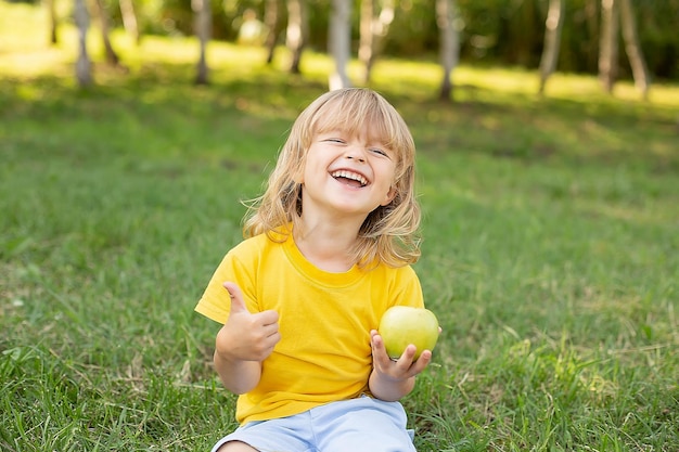 happy boy sitting on the lawn toothy smile in a yellow T-shirt holding a green apple