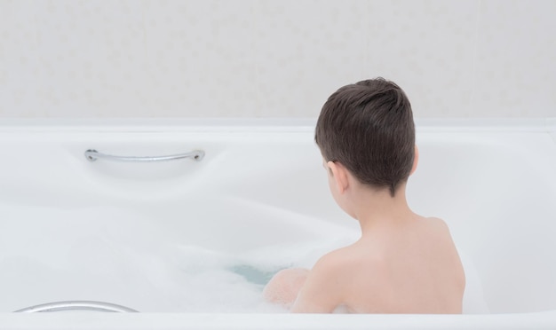 Счастливый мальчик принимает ванну с пышной пеной, играя с пузырьками Концепция здравоохранения личной гигиены