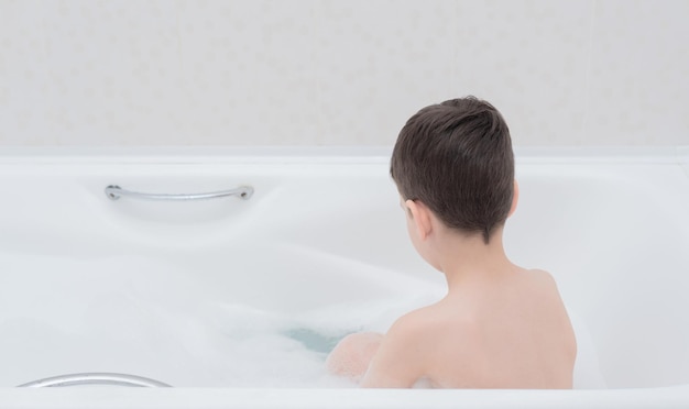 Happy boy takes a bath with lush foam playing with bubbles Personal hygiene healthcare concept