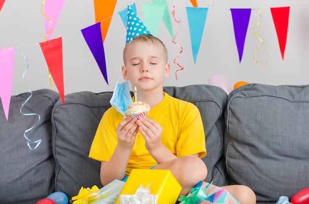 Happy boy took off his face mask, holding holiday cupcake makes wish