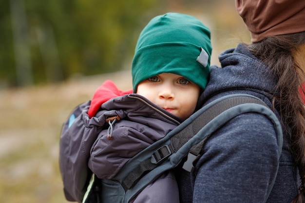 A happy boy travels behind his mother in a baby carrier