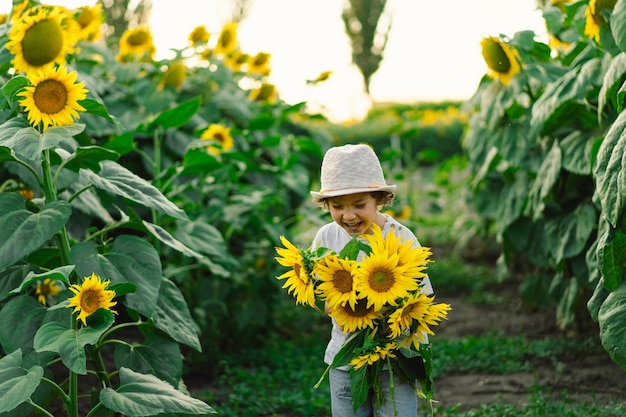 Ragazzo felice che cammina nel campo dei girasoli bambino che gioca con un grande fiore e si diverte